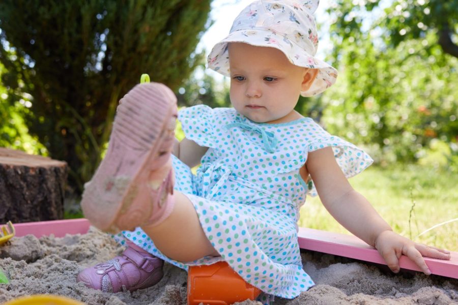 cute little girl playing in sand in sandbox with various toys on outdoor playground