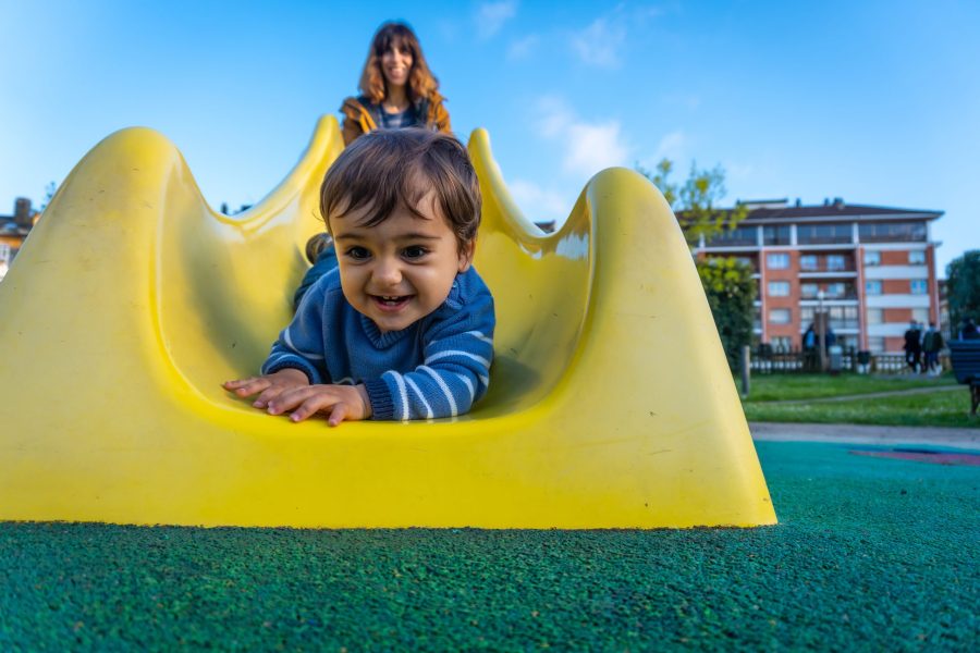 One year old Caucasian boy playing swings with his mother, playing in the park jumping on a yellow squeaker